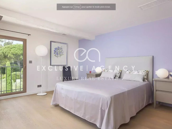 Bedroom with lavender accent wall and a large bed, two nightstands with globe lamps, and a balcony door opening to greenery.
