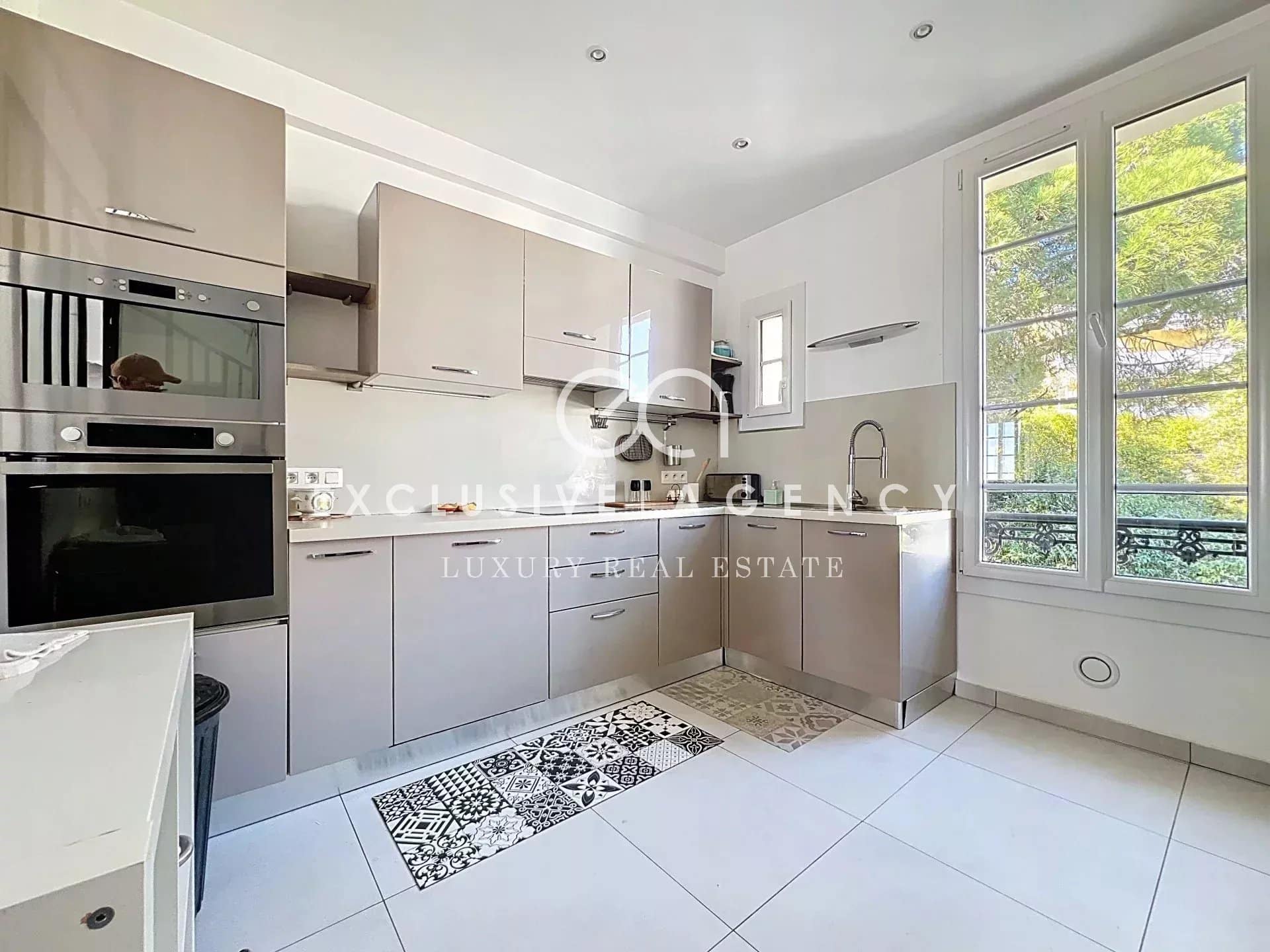 Modern kitchen in a Cannes apartment with light-colored furniture and decorative tiled flooring.