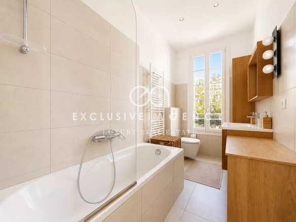 Salle de bain moderne avec baignoire et meuble en bois, lumière naturelle à travers les fenêtres.
