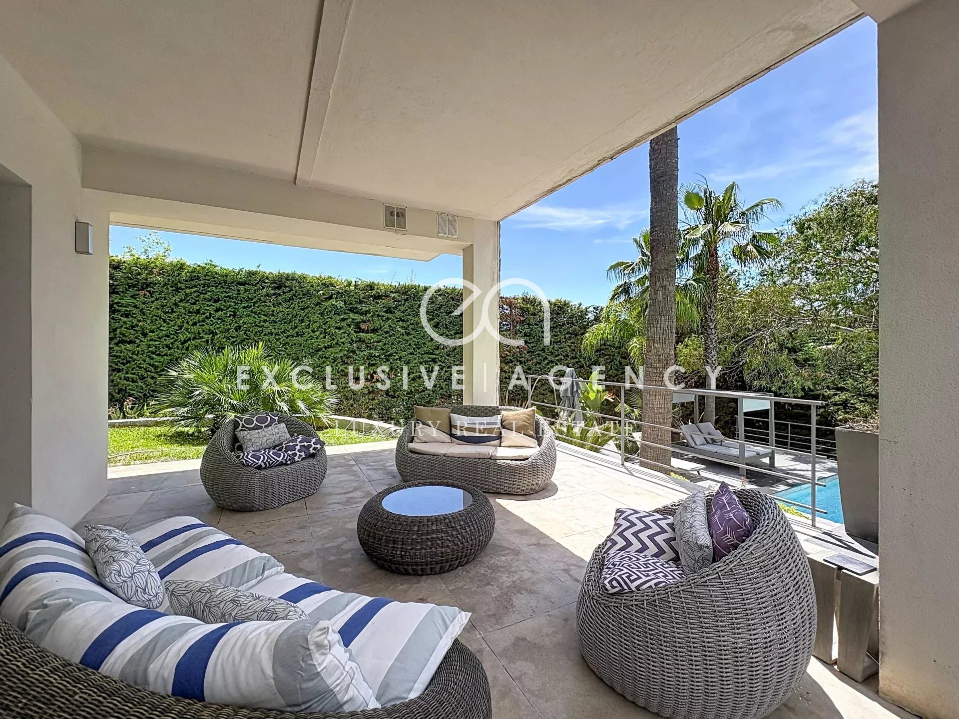 Terrasse d'une villa californienne à Cannes avec mobilier extérieur et piscine visible en arrière-plan.