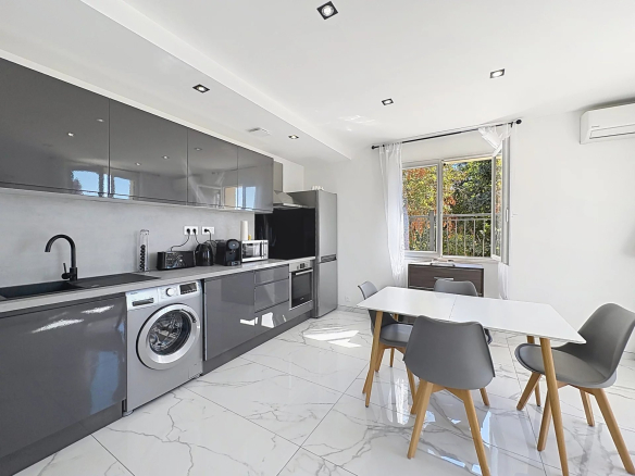 Modern kitchen with grey furniture and a dining area, natural light through a window.