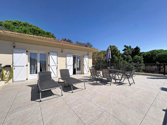 Sunny terrace with sun loungers and table in Cannes, surrounded by greenery.