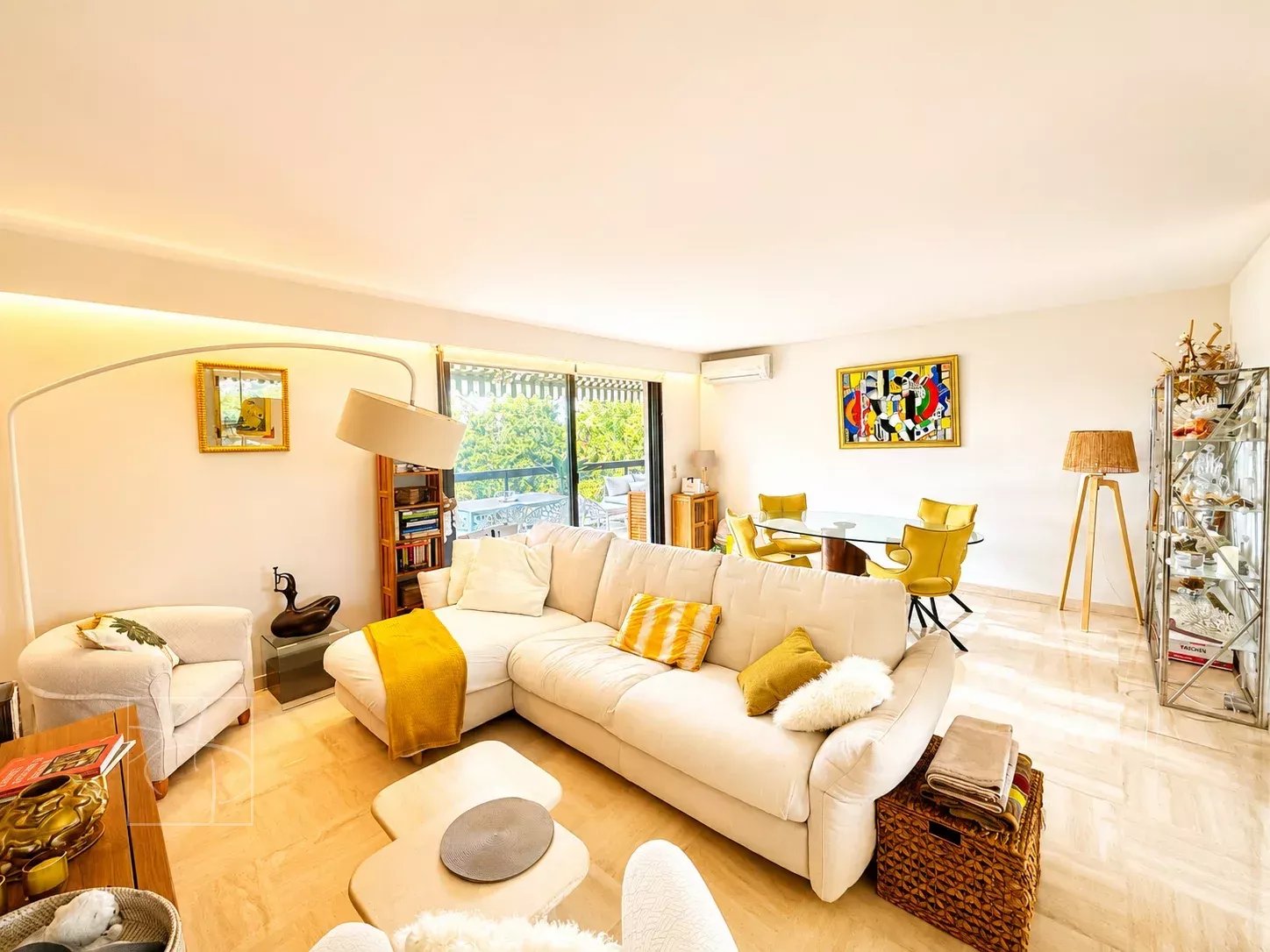 Salon lumineux d'un appartement rénové avec canapé blanc, table à manger et accès à une terrasse.