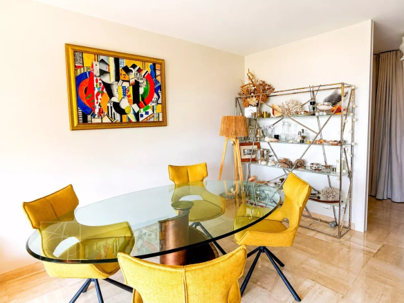 Salle à manger avec table en verre et chaises jaunes dans un appartement rénové à Cannes.