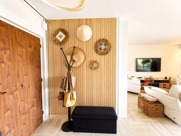 Entrée d'un appartement rénové avec décoration murale en chapeaux et meuble de rangement.