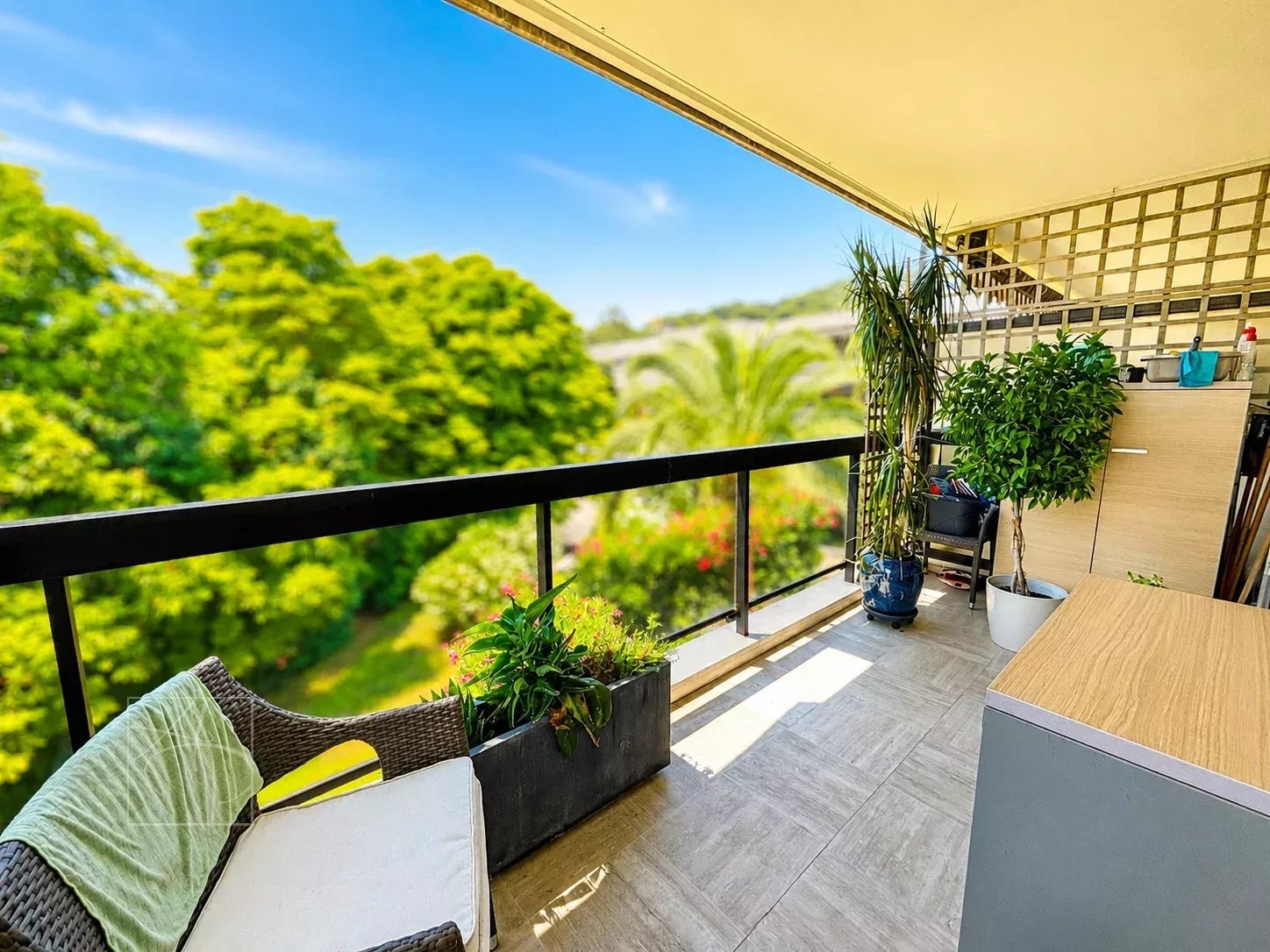 Terrasse d'un appartement à Cannes avec vue sur un parc verdoyant et ciel bleu.