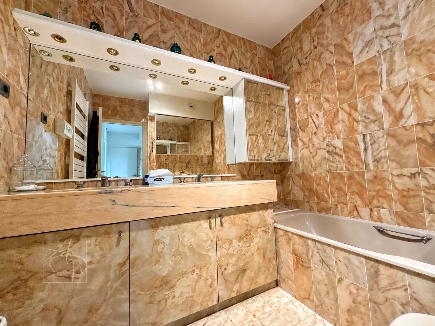 Apartment bathroom with bathtub and mirror, beige marble walls.