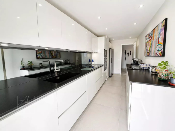 Cuisine moderne et lumineuse d'un appartement à Cannes, avec plans de travail en noir et meubles blancs.
