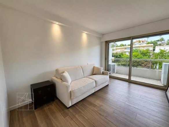 Intérieur d'un appartement moderne avec un canapé et une grande baie vitrée donnant sur un espace extérieur.