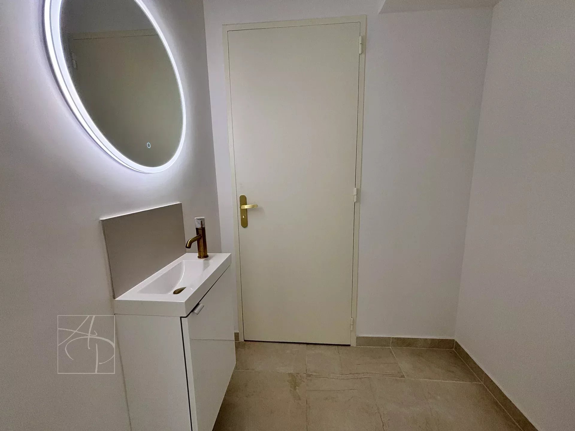 Modern bathroom with round mirror and vanity unit, white walls and beige tiles.