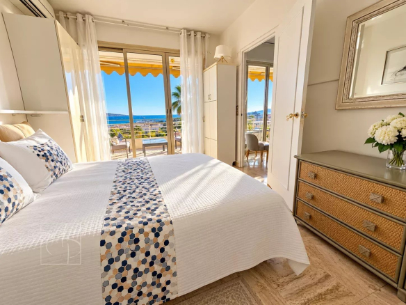 Chambre d'un appartement avec vue mer à Cannes, fenêtres ouvertes sur une terrasse ensoleillée.