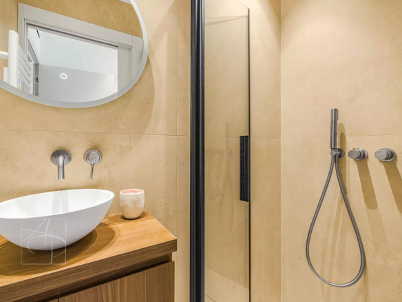Modern bathroom with shower, washbasin on wooden unit and round mirror.