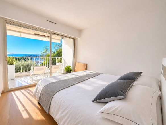 Chambre d'un appartement rénové à Cannes avec vue sur la mer et accès à un balcon.