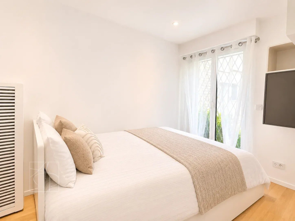 Chambre d'un appartement rénové à Cannes, avec lit double et fenêtres donnant sur l'extérieur.