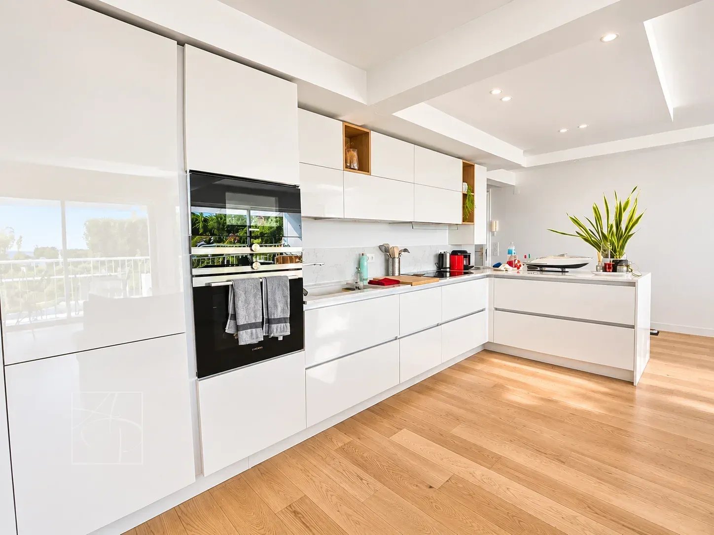 Cuisine moderne et lumineuse d'un appartement rénové à Cannes, avec meubles blancs et parquet en bois.