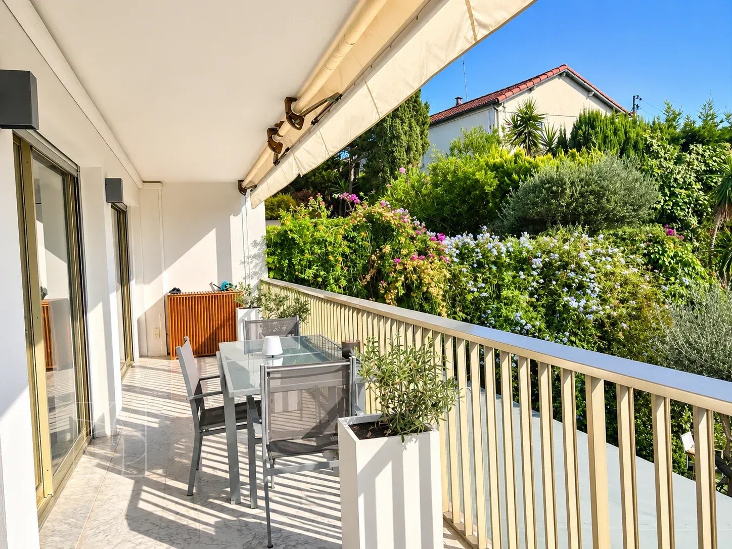 Terrasse d'un appartement rénové à Cannes avec vue sur des jardins fleuris.
