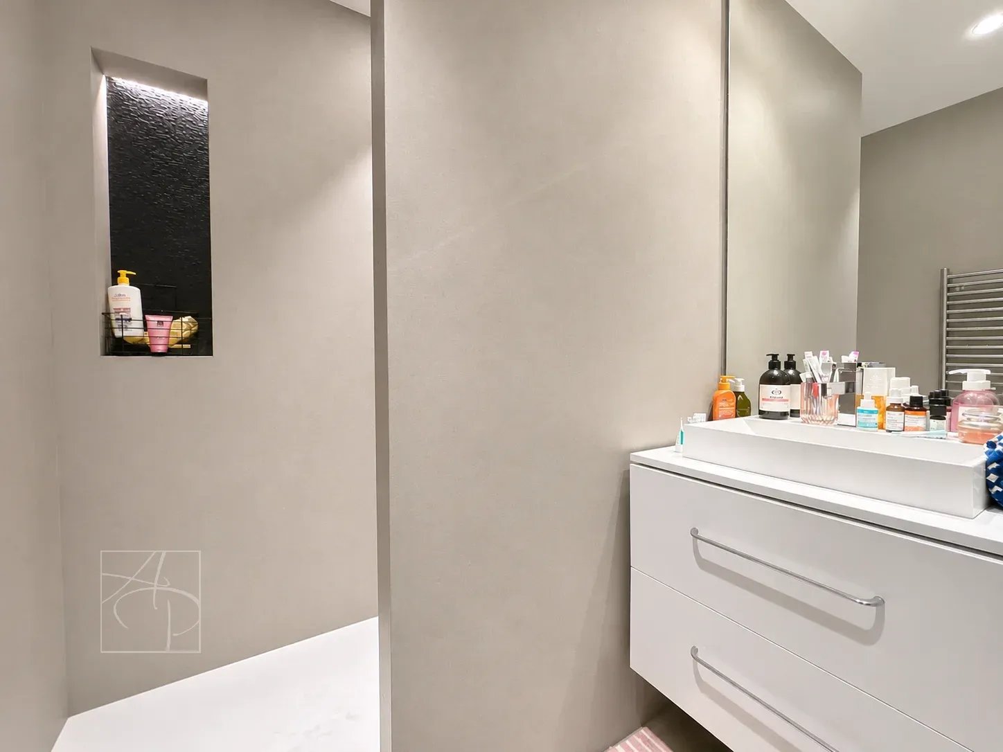 Salle de bain moderne avec douche et meuble de rangement, murs en teintes neutres.