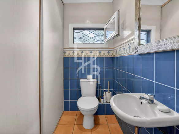 Compact bathroom with blue tile walls, orange floor, and white toilet and sink; small window above the toilet is open.