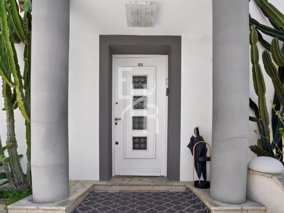 White front door framed by a gray entryway with two large columns and tall cacti on both sides.