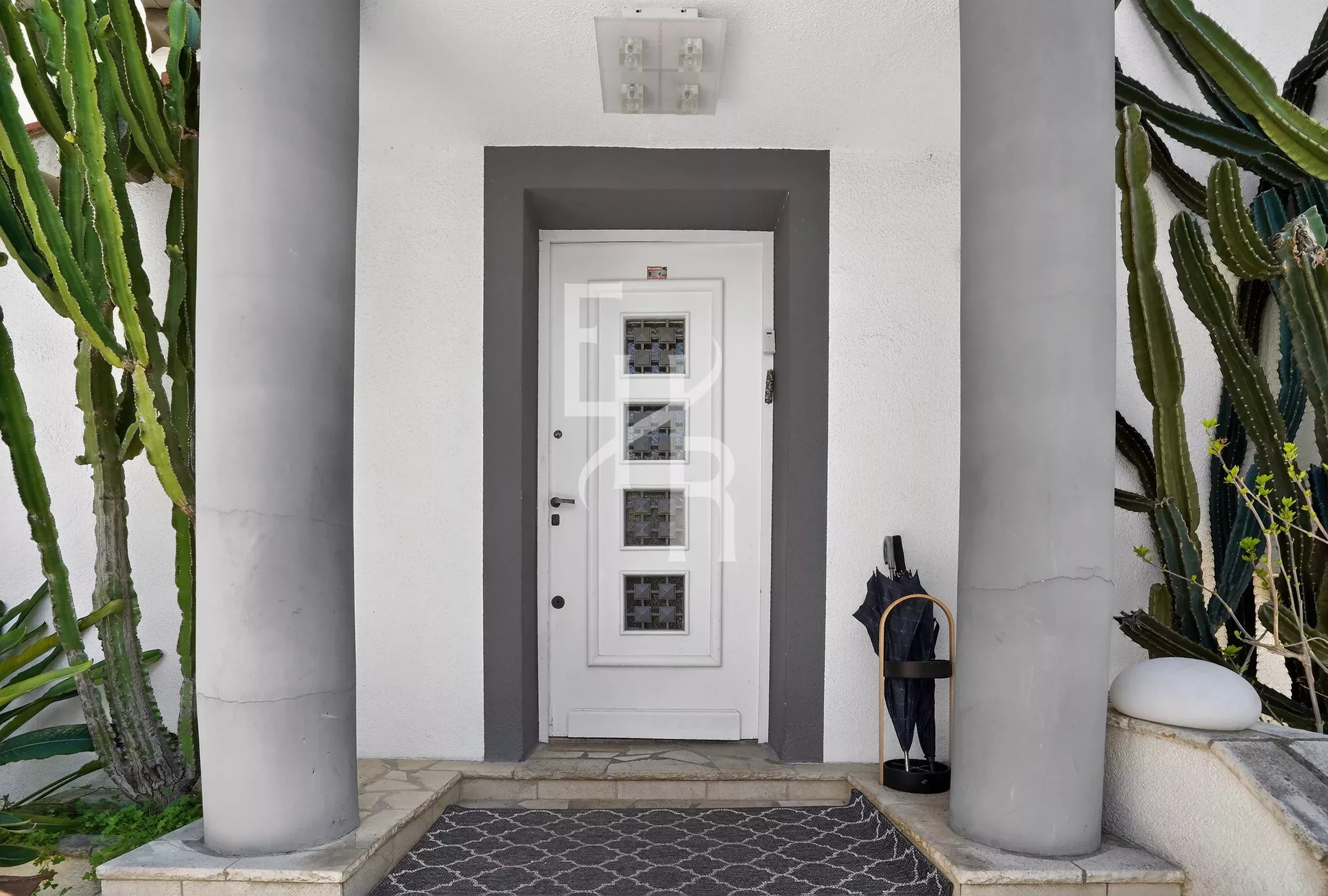 White front door framed by a gray entryway with two large columns and tall cacti on both sides.