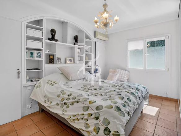 White bedroom with built-in shelving behind the bed, bust sculptures, framed photos, and a botanical duvet on a low bed.
