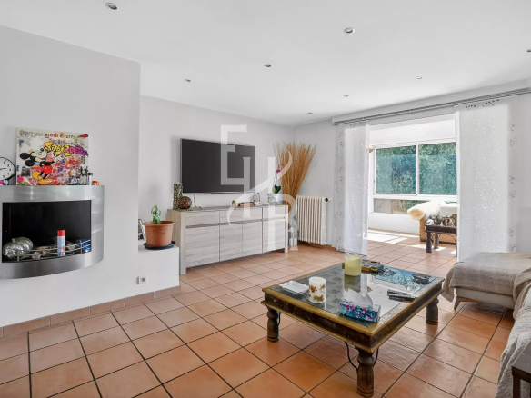 Bright living room with a wall-mounted flat-screen TV over a white cabinet, a fireplace to the left, and terracotta tile flooring under a glass coffee table and sofa setup.
