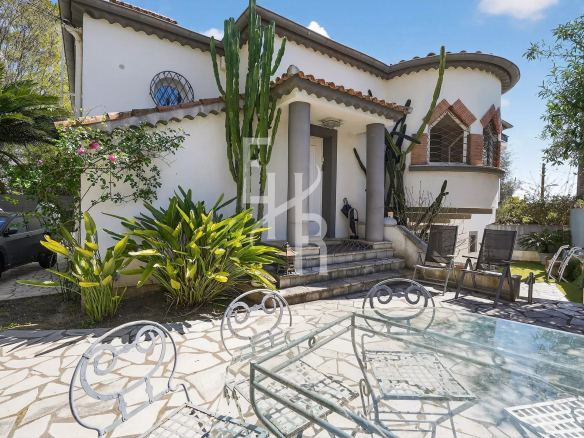 White house with rounded tower and tall cacti at the entrance, stone steps, and a glass-top patio table with iron chairs in a sunny backyard.