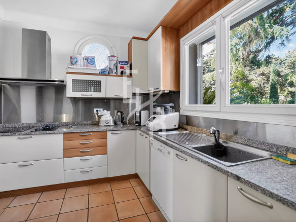 Bright L-shaped kitchen with white cabinets, granite countertops, and a large window overlooking greenery; sink and appliances along the counter.