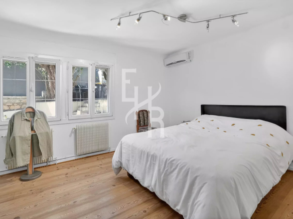 Bright minimalist bedroom with a white bed, light wood floor, and large windows letting in natural light.