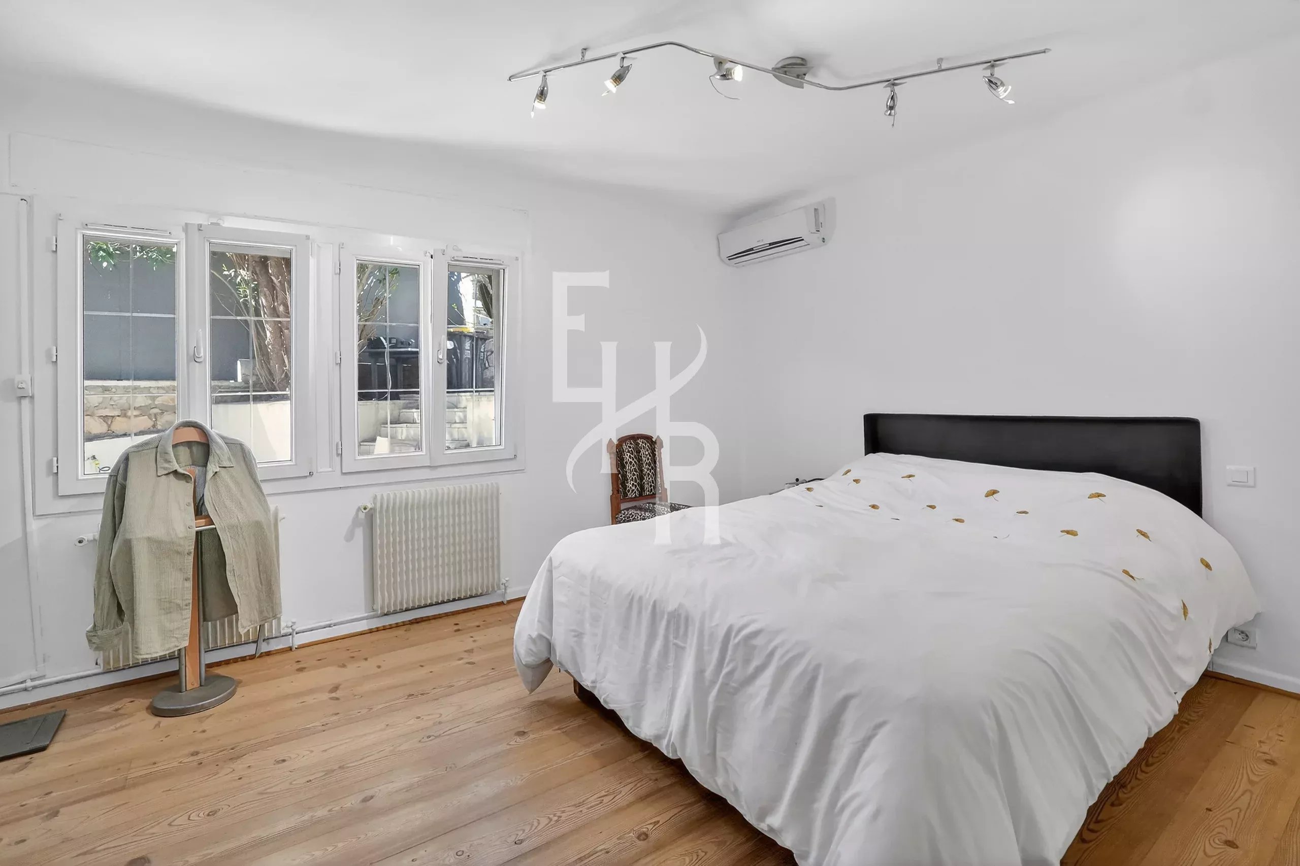 Bright minimalist bedroom with a white bed, light wood floor, and large windows letting in natural light.