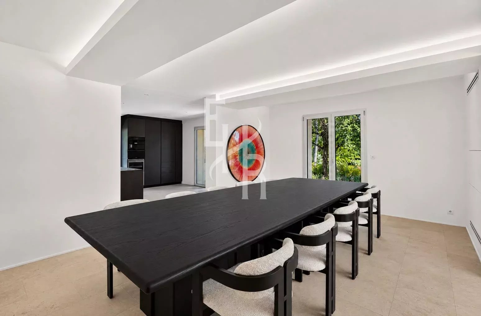 Salle à manger moderne à Mougins Salle à manger moderne avec une grande table noire et des chaises claires, donnant sur un jardin.