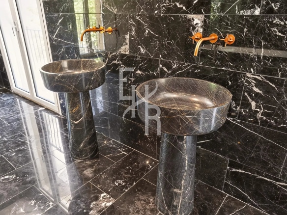 Salle de bains avec deux lavabos en marbre noir et robinets dorés.