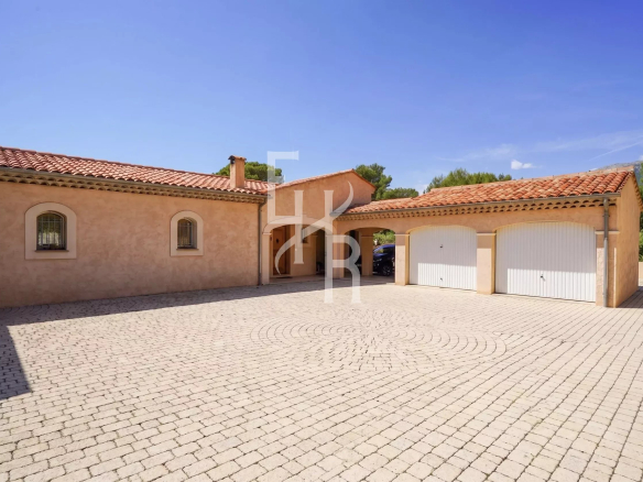 Single-storey villa with garage and paved courtyard in Cabris, surrounded by greenery.
