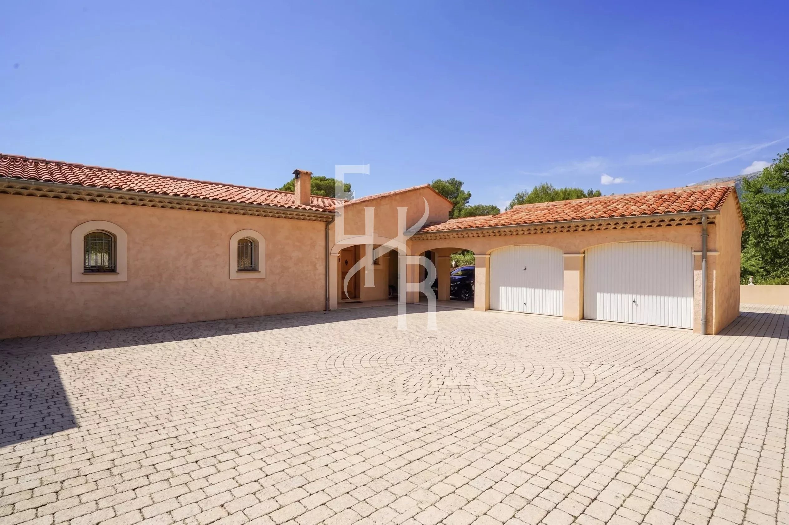 Single-storey villa with garage and paved courtyard in Cabris, surrounded by greenery.