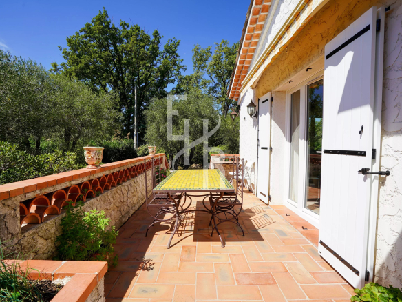 Terrasse ensoleillée d'une villa provençale avec table et chaises, entourée d'arbres.