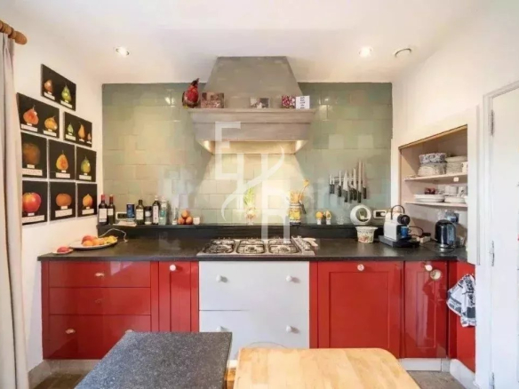 Cuisine d'un mas provençal en pierre à Mougins, avec meubles rouges et plan de travail en pierre.