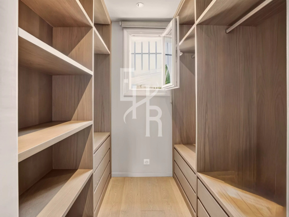 Interior of a spacious dressing room with shelves and drawers, natural light entering through a window.