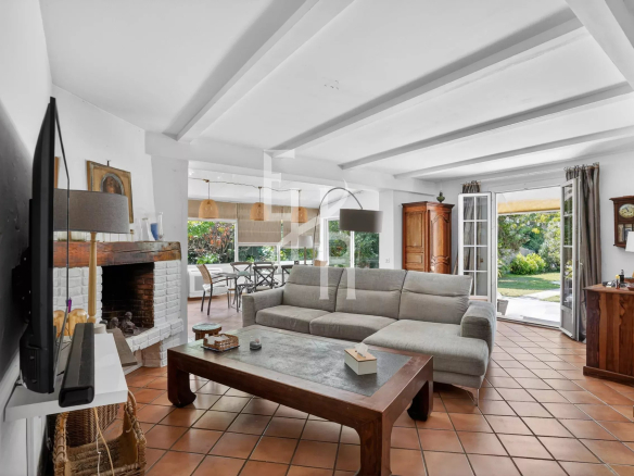 Intérieur d'une villa avec un salon spacieux, canapé et cheminée, donnant sur un jardin.