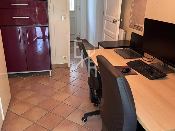 Intérieur d'un bureau avec deux chaises et un ordinateur, murs clairs et meubles sombres.