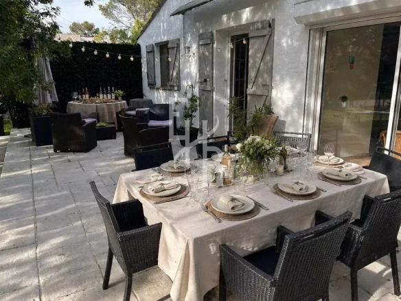 Terrasse d'une villa avec une table dressée pour un repas en extérieur, chaises noires et décor floral.