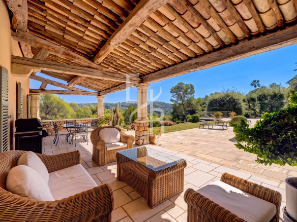 Terrasse ensoleillée avec mobilier en osier et vue sur le jardin verdoyant d'une villa à Mougins.