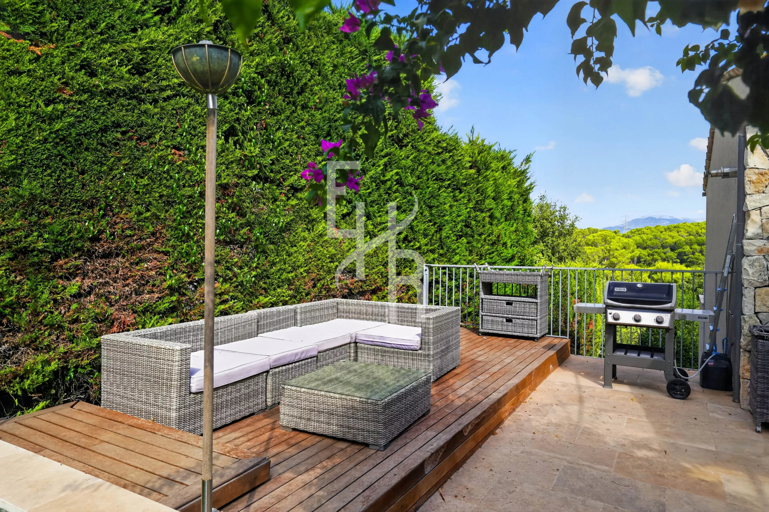 Terrasse en bois avec mobilier de jardin et barbecue, entourée de verdure à Mougins.