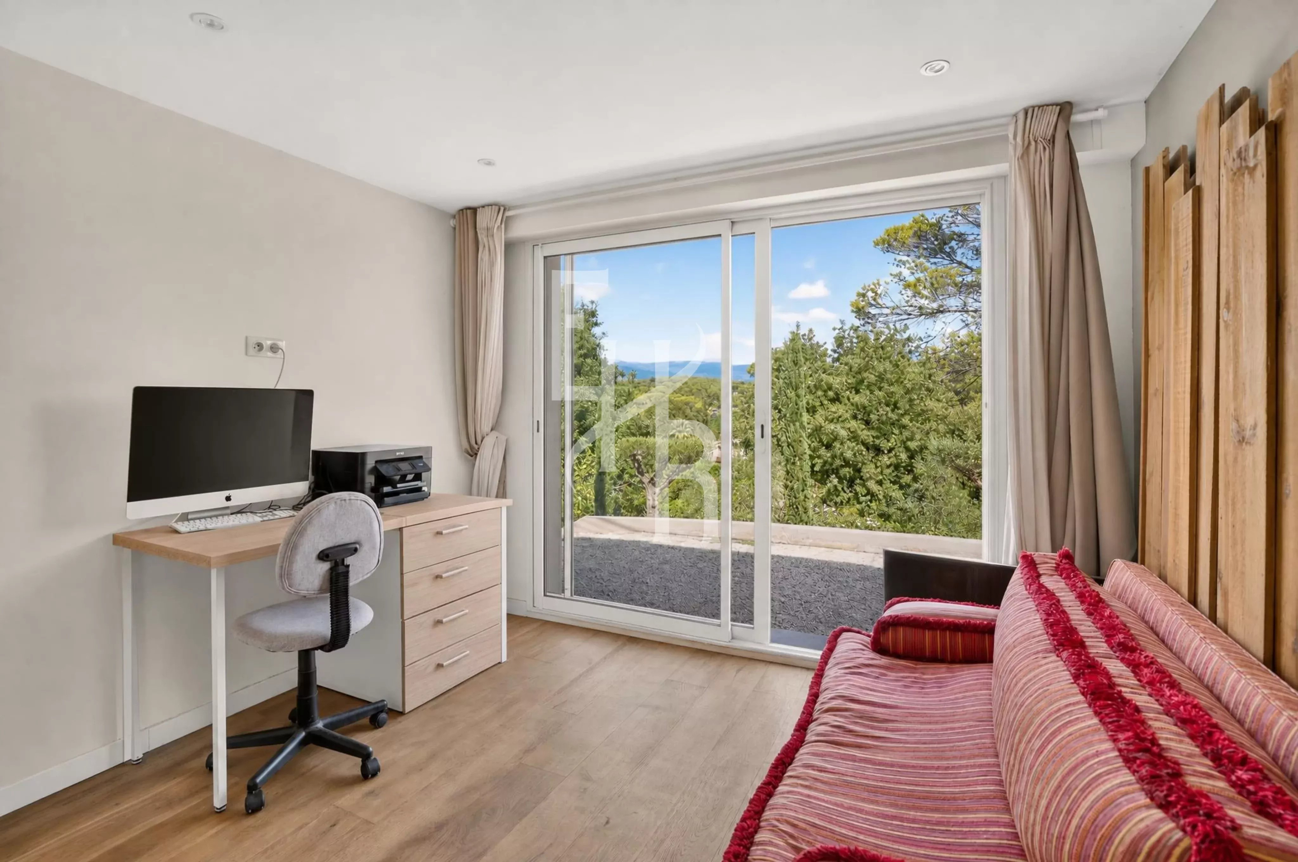 Intérieur d'une villa à Mougins avec bureau, canapé et vue sur la nature.