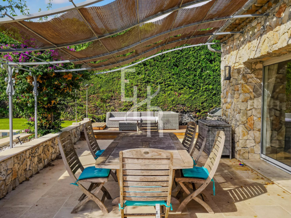 Terrasse en pierre avec table en bois et chaises, entourée de verdure dans un domaine à Mougins.