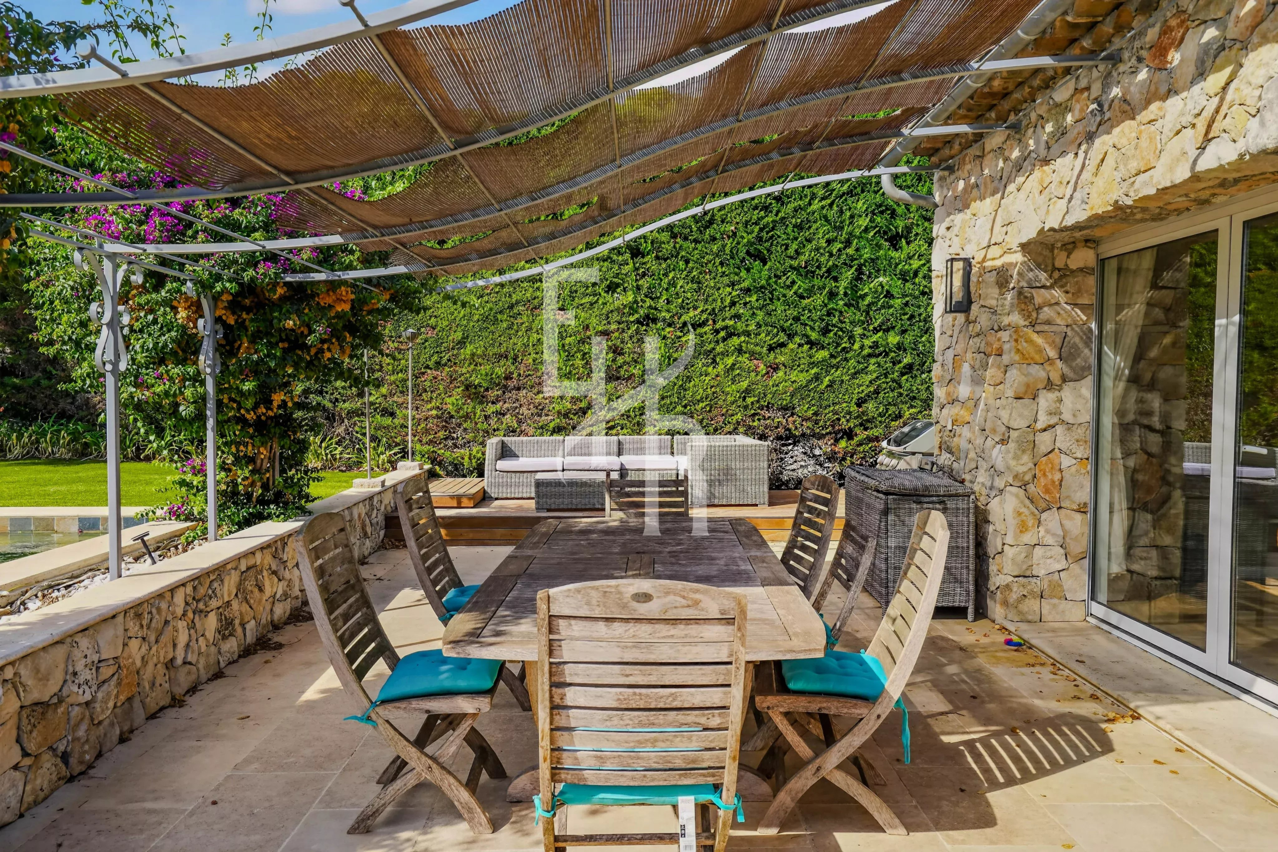 Terrasse en pierre avec table en bois et chaises, entourée de verdure dans un domaine à Mougins.