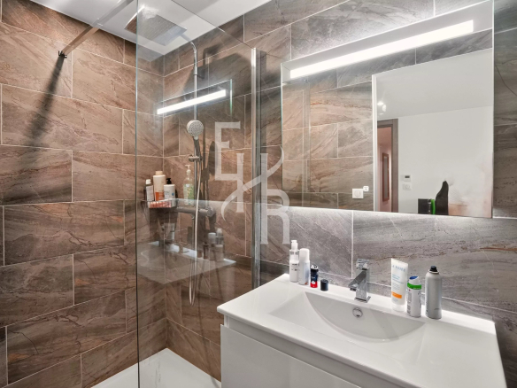 Salle de bain moderne avec douche en verre et lavabo, décorée de carreaux en pierre.