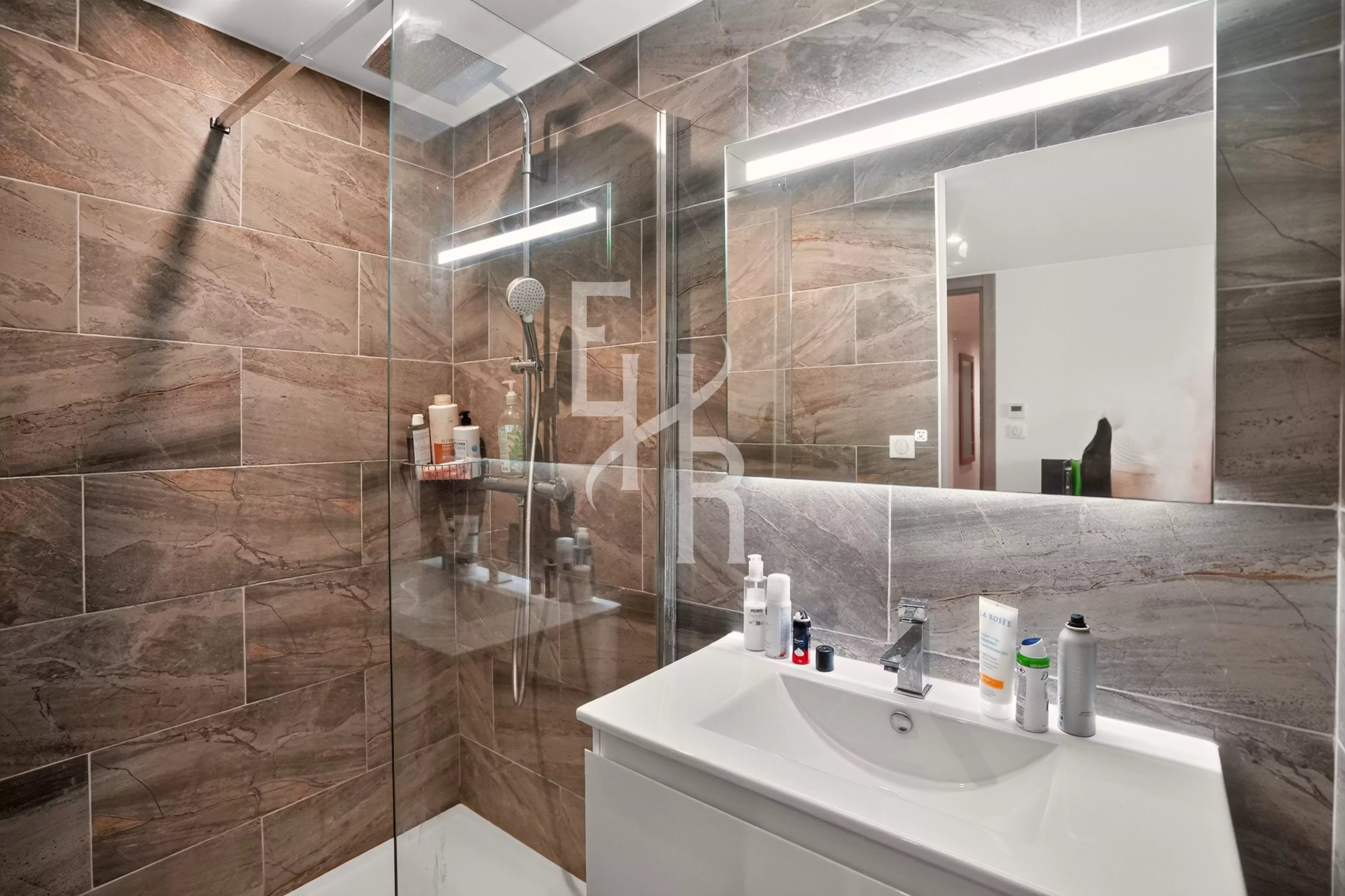 Salle de bain moderne avec douche en verre et lavabo, décorée de carreaux en pierre.