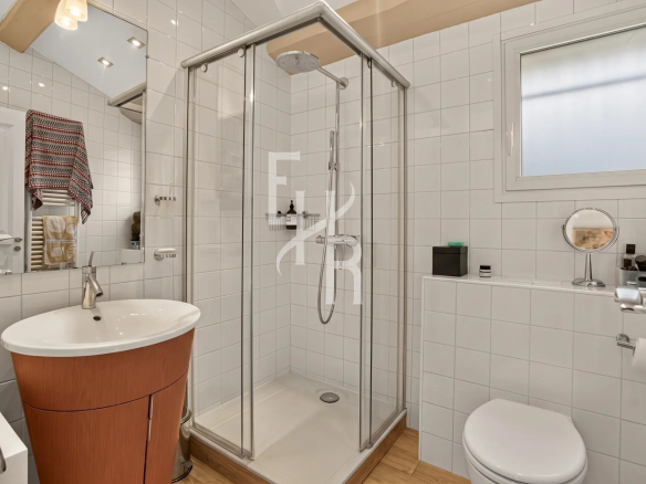 Salle de bain moderne avec douche, lavabo et toilettes, carrelage blanc et bois.