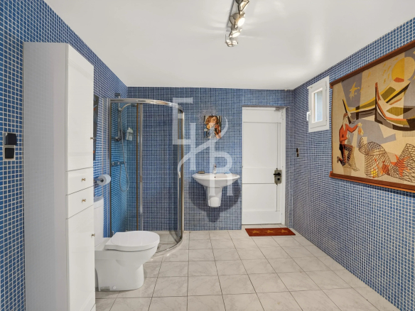 Salle de bain avec carrelage bleu, douche, lavabo et décoration murale à Mougins.