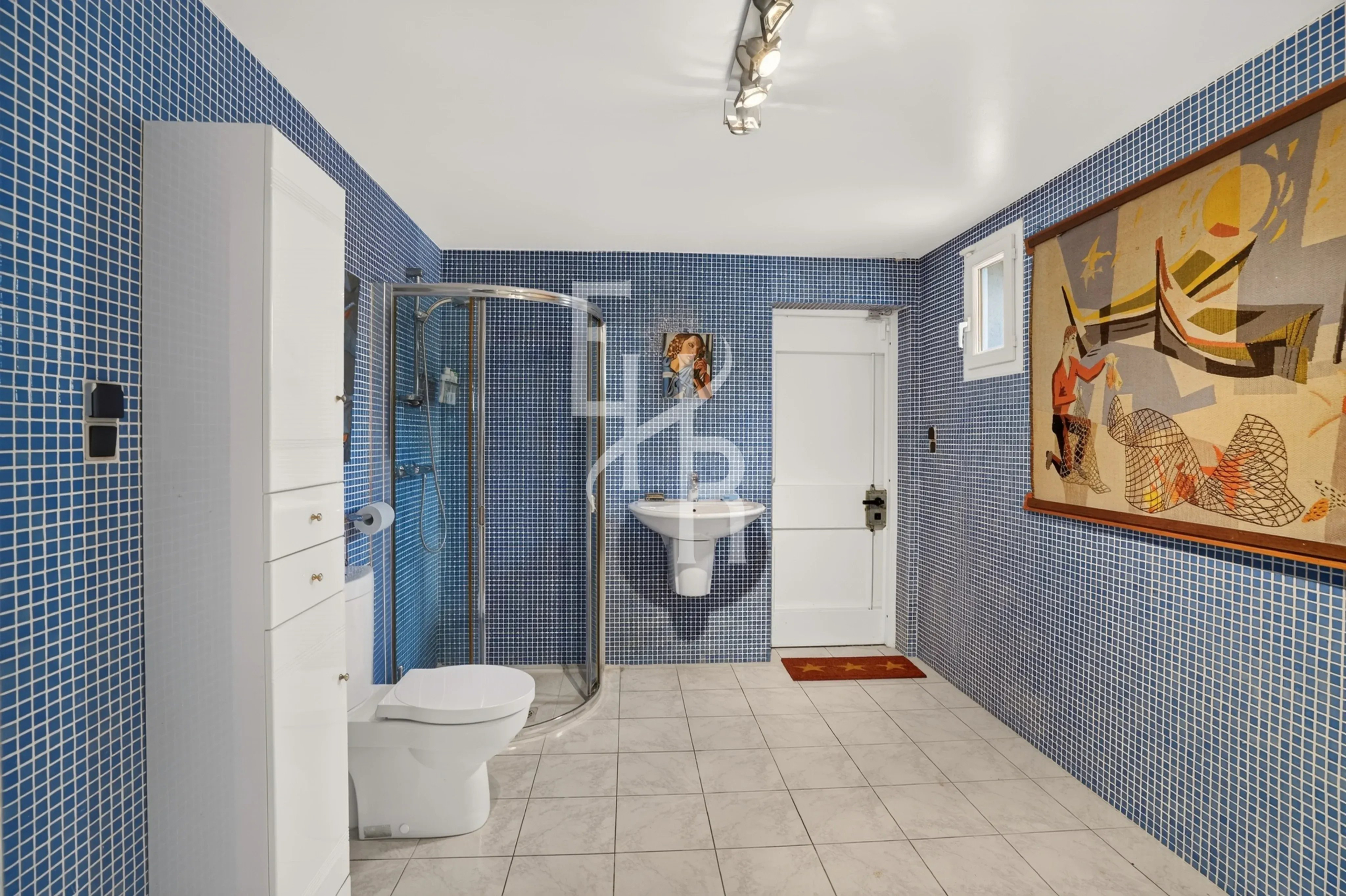 Salle de bain élégante à Mougins Salle de bain avec carrelage bleu, douche, lavabo et décoration murale à Mougins.